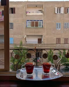 two cups of tea sit on a tray in front of a window overlooking an apartment building