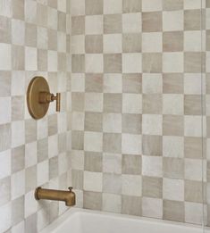 a bath tub sitting next to a tiled wall with gold fixtures on the faucet