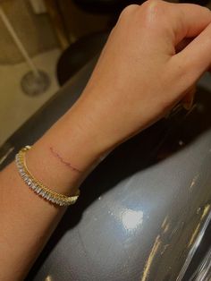 a woman's arm with a small tattoo on it and a gold bracelet around her wrist