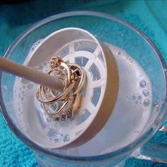 there is a ring holder in the middle of a glass container with water and gold rings on it