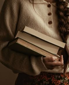 a woman holding two books in her hands and looking down at the book she is holding