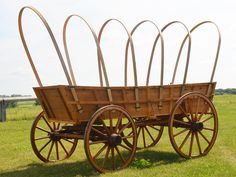 an old wooden wagon sitting in the middle of a grassy field with four spoked wheels