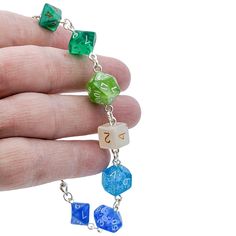 a hand is holding some dice necklaces on it's fingers and the beads are green, blue, and white