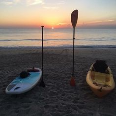 two kayaks sitting on the beach at sunset with paddles leaning up against them