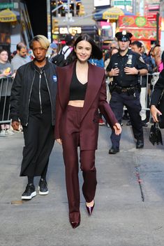 a woman walking down the street in a maroon suit and matching heels with police officers