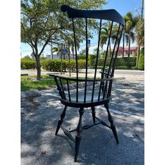 a black chair sitting in the middle of a parking lot next to trees and grass