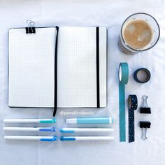 an open notebook, pens, and other office supplies are laid out on a table