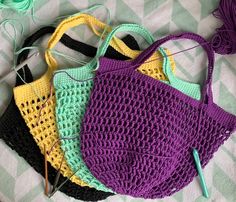 four crocheted purses are sitting on a table with yarn and needles in them