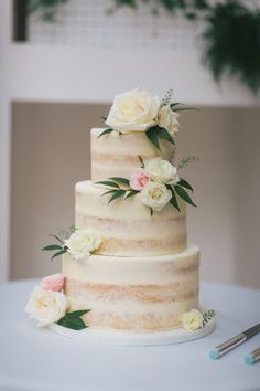 a three tiered cake with white and pink flowers on the top is ready to be cut