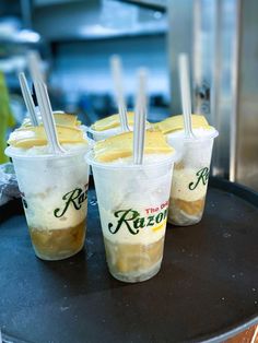 four plastic cups with straws in them on top of a black tray next to other food items