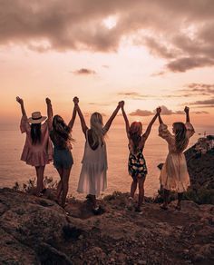 four girls standing on top of a hill with their arms in the air and one girl holding her hands up