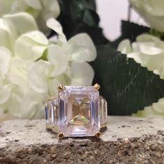 an engagement ring with a fancy pink diamond surrounded by white flowers and greenery in the background