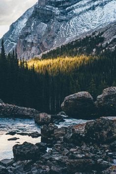 there is a river in the mountains with rocks and trees on both sides that are surrounded by large boulders