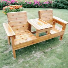 two wooden chairs sitting on top of a green grass covered field next to pink flowers