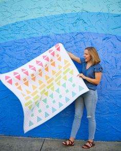 a woman holding up a colorful quilt against a blue wall