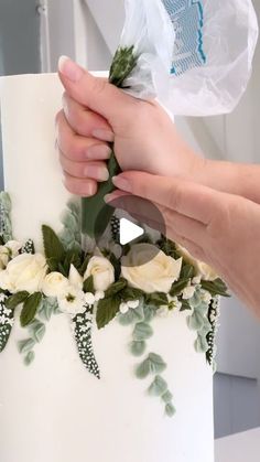 a person is decorating a wedding cake with white flowers and greenery on it