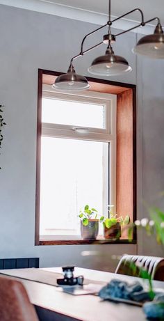 a dining room table with chairs and potted plants on the window sill next to it