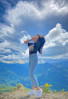 a woman standing on top of a mountain with her arms in the air and looking up