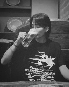 a person sitting at a table with a glass in front of their face, drinking from a mug