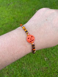 a person wearing a bracelet with an orange button on it's wrist and a beaded pumpkin charm