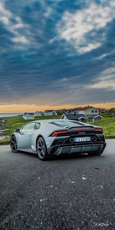 a silver sports car parked on the side of a road next to some grass and houses