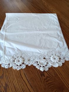 a white table cloth with crochet lace on it sitting on a wooden floor