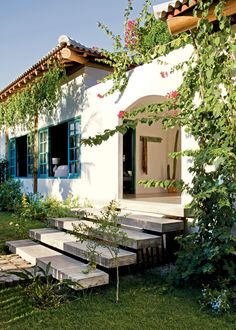 a white house with blue windows and green shutters on the outside, surrounded by greenery