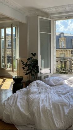 an unmade bed sitting in front of two large windows on top of a wooden floor