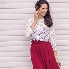 a woman standing in front of a white wall talking on a cell phone and smiling