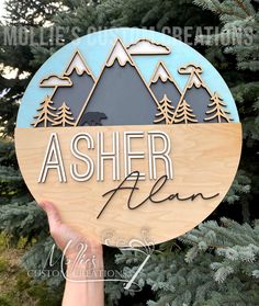 a person holding up a wooden sign with the words asher place in front of some trees