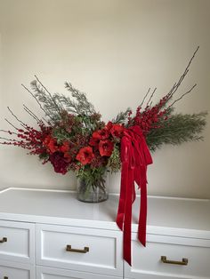 a vase filled with red flowers on top of a white dresser