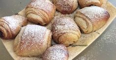 a bunch of pastries sitting on top of a wooden tray covered in powdered sugar