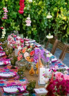 a long table is set with colorful flowers and candles for an outdoor dinner or party