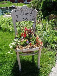 a welcome sign sitting on top of a wooden chair filled with potted plants and flowers