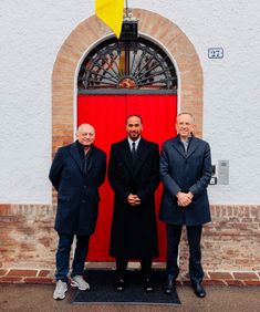 three men standing in front of a red door