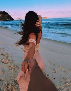 a woman holding the hand of a man on top of a sandy beach next to the ocean