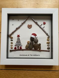 a white frame with some rocks in it and a christmas decoration on the wall behind it