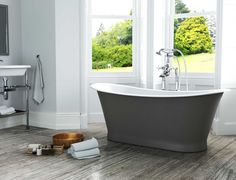 a bath tub sitting next to two windows in a bathroom with wood floors and white walls