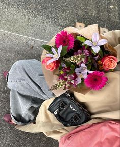 a bouquet of flowers sitting on the ground next to someone's purse and handbag