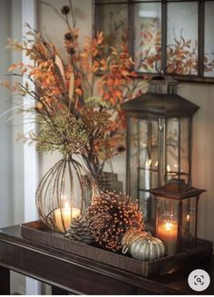 some candles are sitting on top of a mantle with flowers and leaves in vases