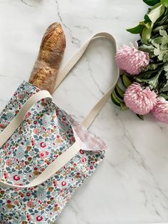 a bag with bread in it sitting next to flowers on a marble counter top,