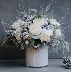 a bouquet of flowers in a white vase with pine cones and snow flakes on the side