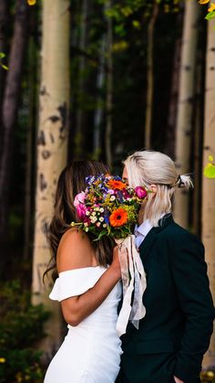 a bride and groom standing in front of trees with flowers on their heads, kissing