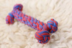 a red and blue rope dog toy laying on top of a white rug with it's tail curled up