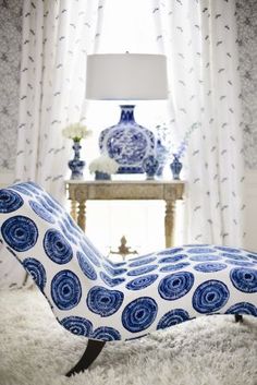 a blue and white chaise lounge chair sitting in front of a window with curtains