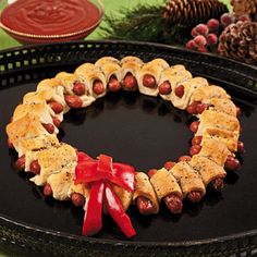 a wreath made out of pigs in a blanket on top of a black plate with red ribbon