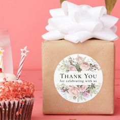 a cupcake next to a gift box with a candle on it and a pink background