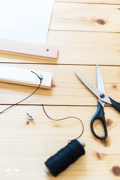 a pair of scissors sitting on top of a wooden table next to thread and glue