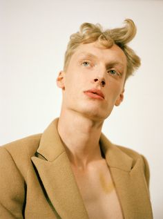 a man with blonde hair wearing a tan blazer and looking up at the camera