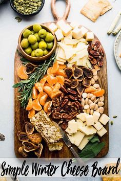 a wooden cutting board topped with cheese and olives next to crackers, nuts and bread